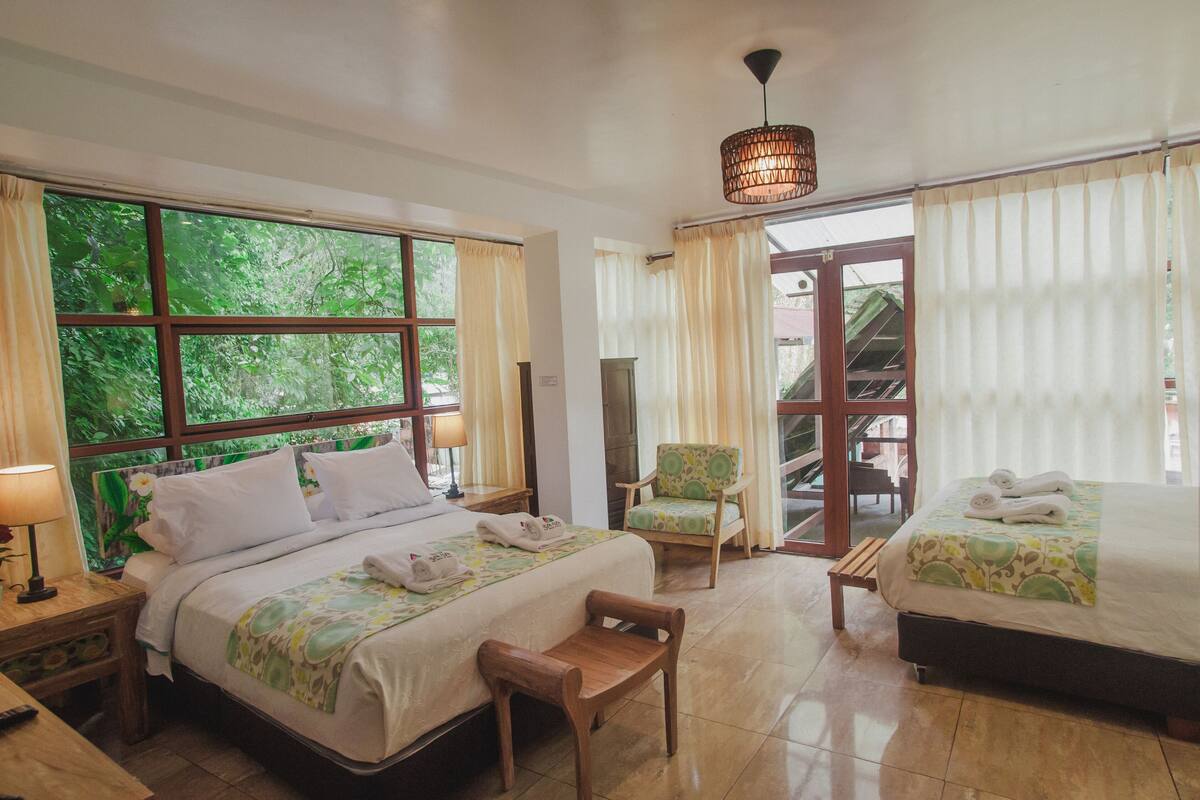 A hotel room with two beds, a chair, a nightstand, and a window with curtains.