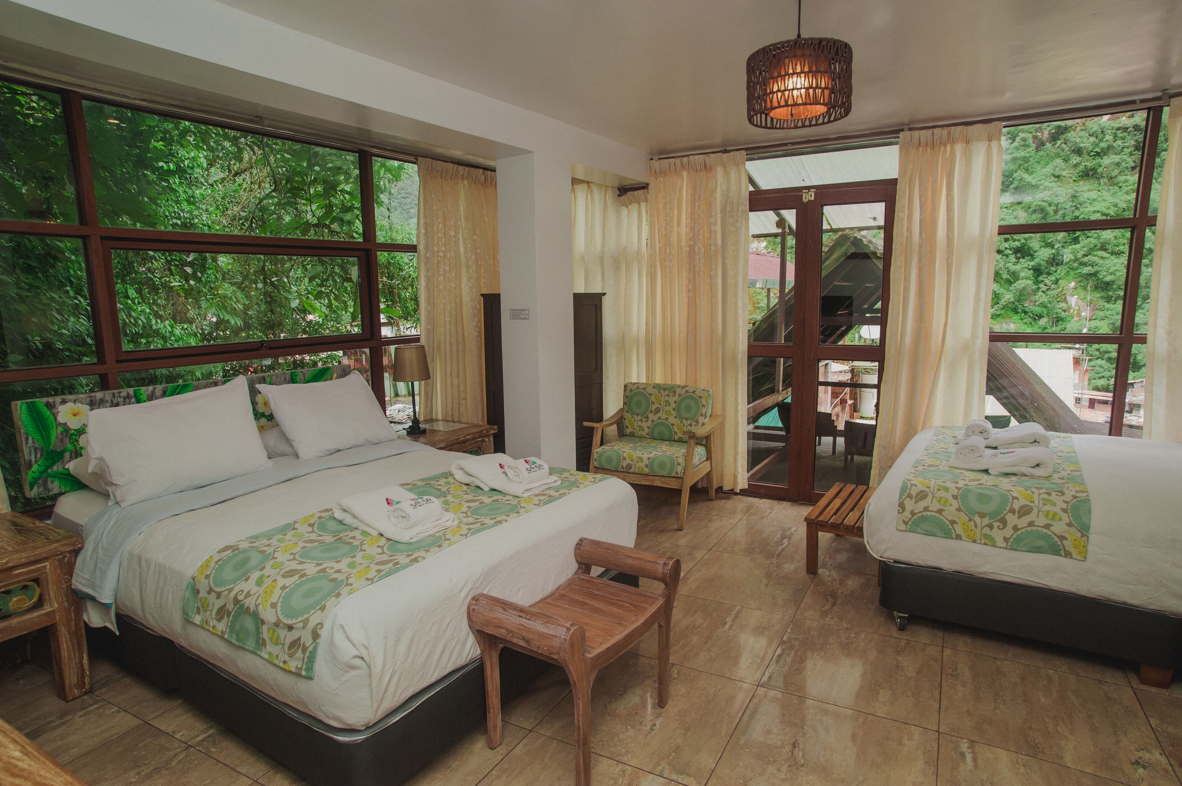 A hotel room with a large bed, a smaller bed, a chair, a wooden bench, and a table.