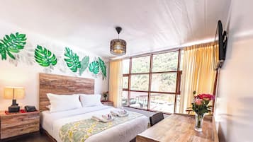 Un dormitorio bien iluminado con una cama de madera, una mesita de noche con una lámpara, un escritorio con un florero y un gran ventanal con cortinas.