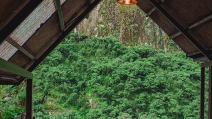 A dining area with wooden tables and chairs, a glass-top table, and a view of a lush green forest through a wooden structure. - Rupa Rupa High Jungle Eco B&B (Machu Picchu)