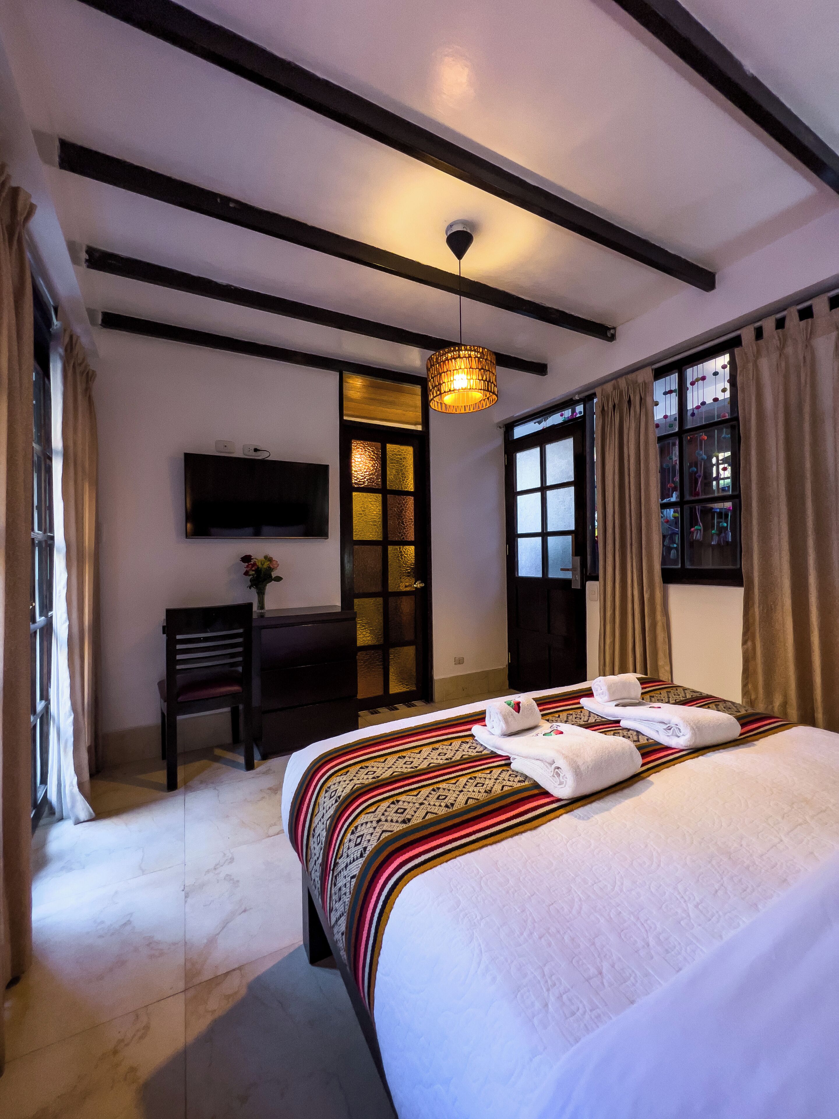 A hotel room with a bed, a desk, a television, and a window with curtains.