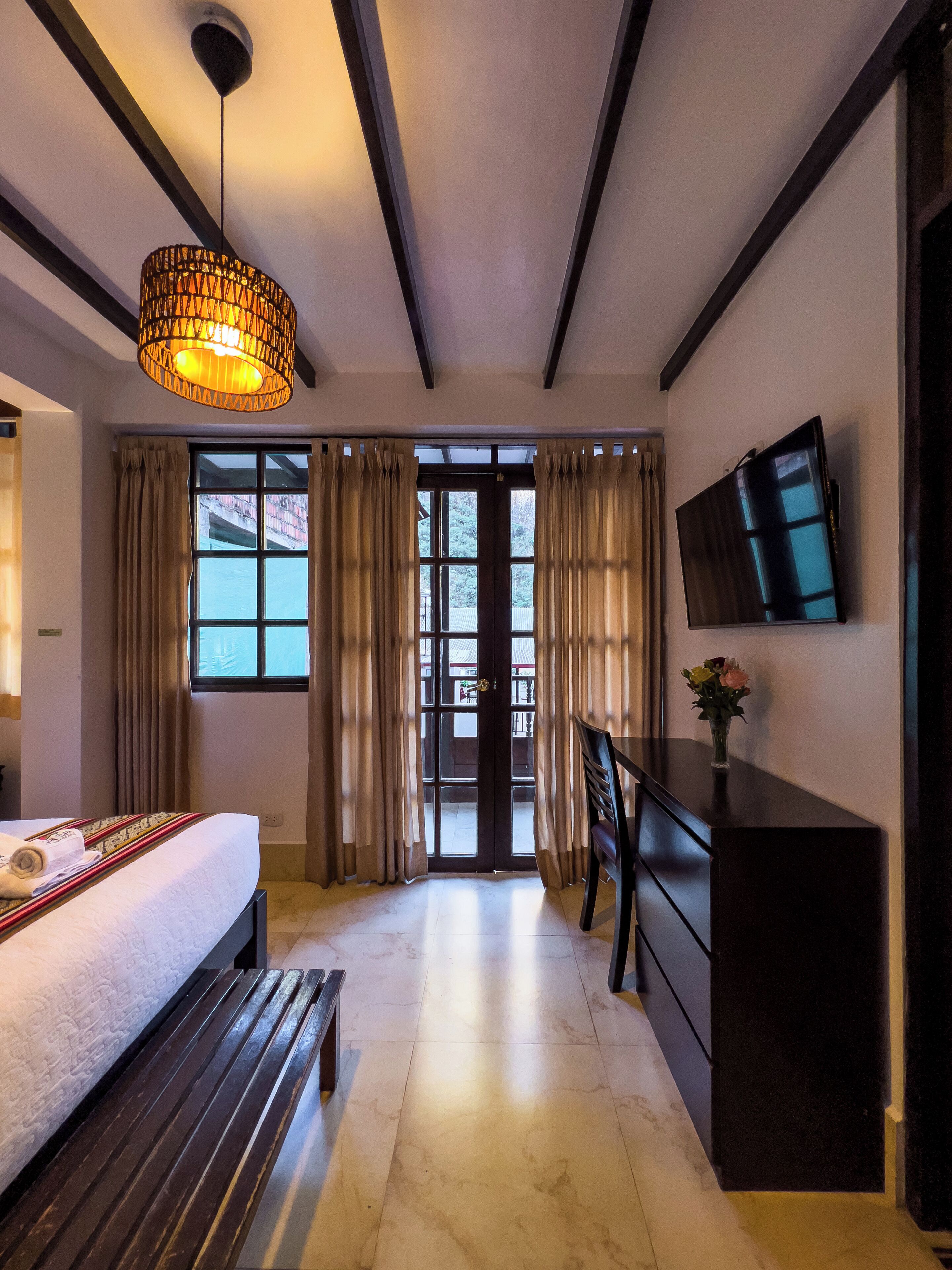 A hotel room with a bed, a desk, a TV, and a window with curtains.