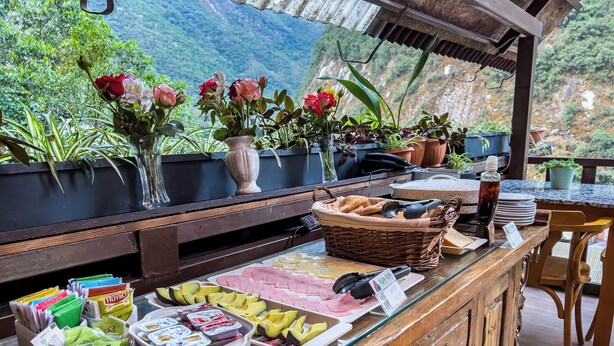A buffet setup with various food items, a wicker basket, and a vase with flowers. - Rupa Rupa High Jungle Eco B&B (Machu Picchu)