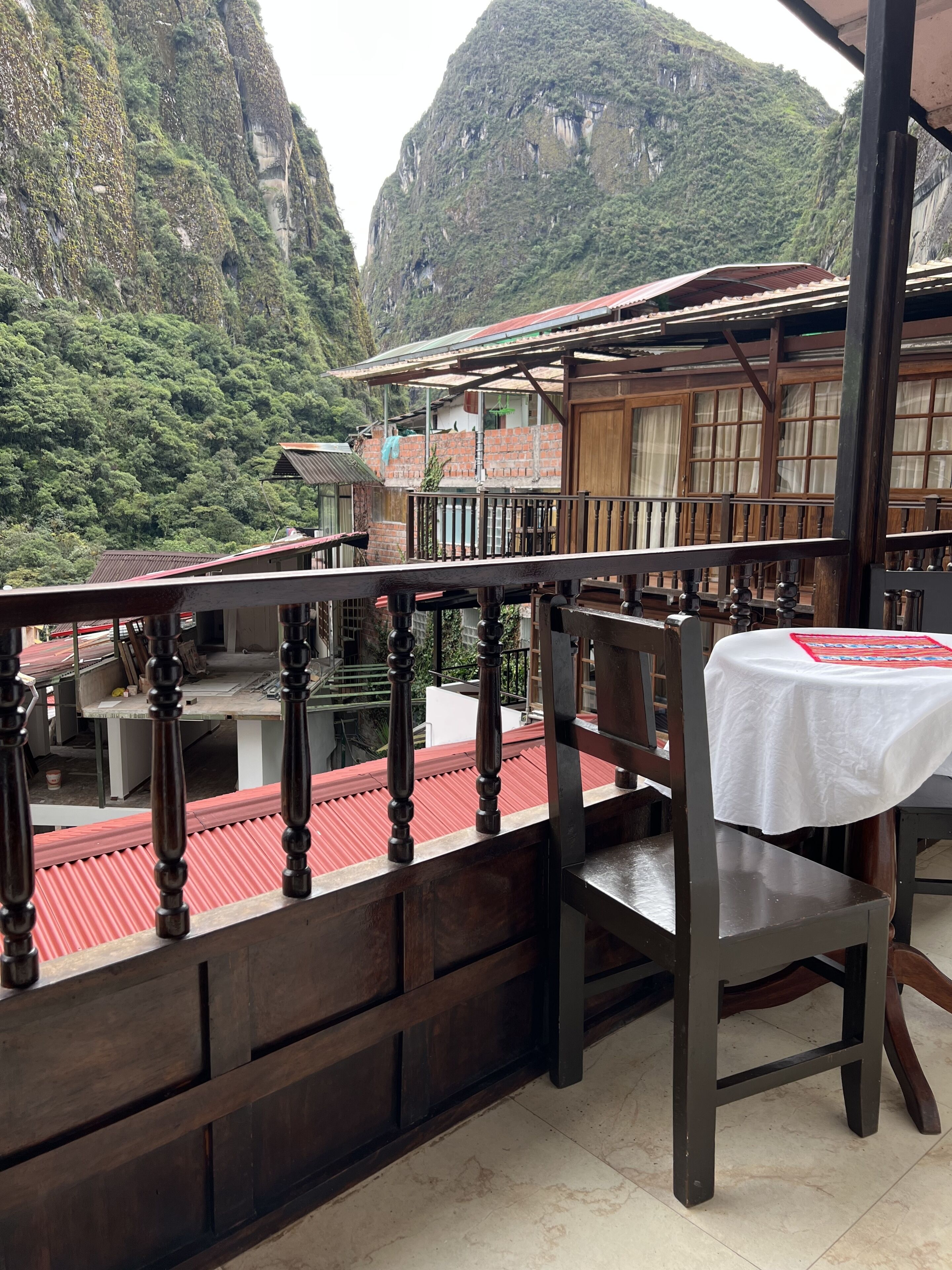 A balcony with a table and chair, overlooking a mountainous landscape with traditional buildings.