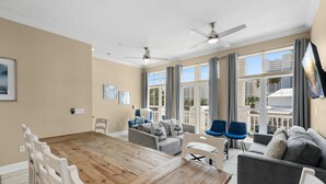 A spacious living room with a wooden dining table, grey sofas, and a ceiling fan. - Pool, A Block To The Beach, Private Elevator, Nearby Fun & Restaurants (Panama City Beach)