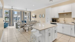 A modern kitchen with white cabinetry, a central island, and a dining area with chairs and a table. - Pool, A Block To The Beach, Private Elevator, Nearby Fun & Restaurants (Panama City Beach)