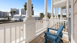 A balcony with white railings and a blue chair, overlooking a cityscape with tall buildings and palm trees. - Pool, A Block To The Beach, Private Elevator, Nearby Fun & Restaurants (Panama City Beach)