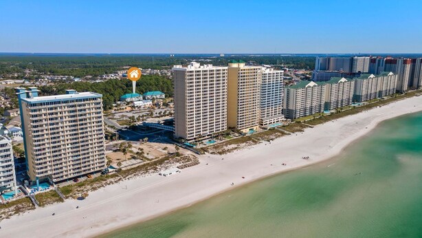 A coastal hotel area with multiple high-rise buildings, a sandy beach, and a clear blue sky. - Pool, A Block To The Beach, Private Elevator, Nearby Fun & Restaurants (Panama City Beach)