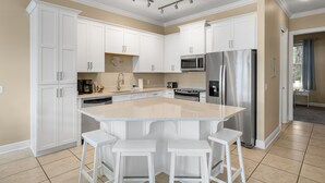 A modern kitchen with white cabinets, a large island with bar stools, stainless steel appliances, and a beige color scheme. - Pool, A Block To The Beach, Private Elevator, Nearby Fun & Restaurants (Panama City Beach)