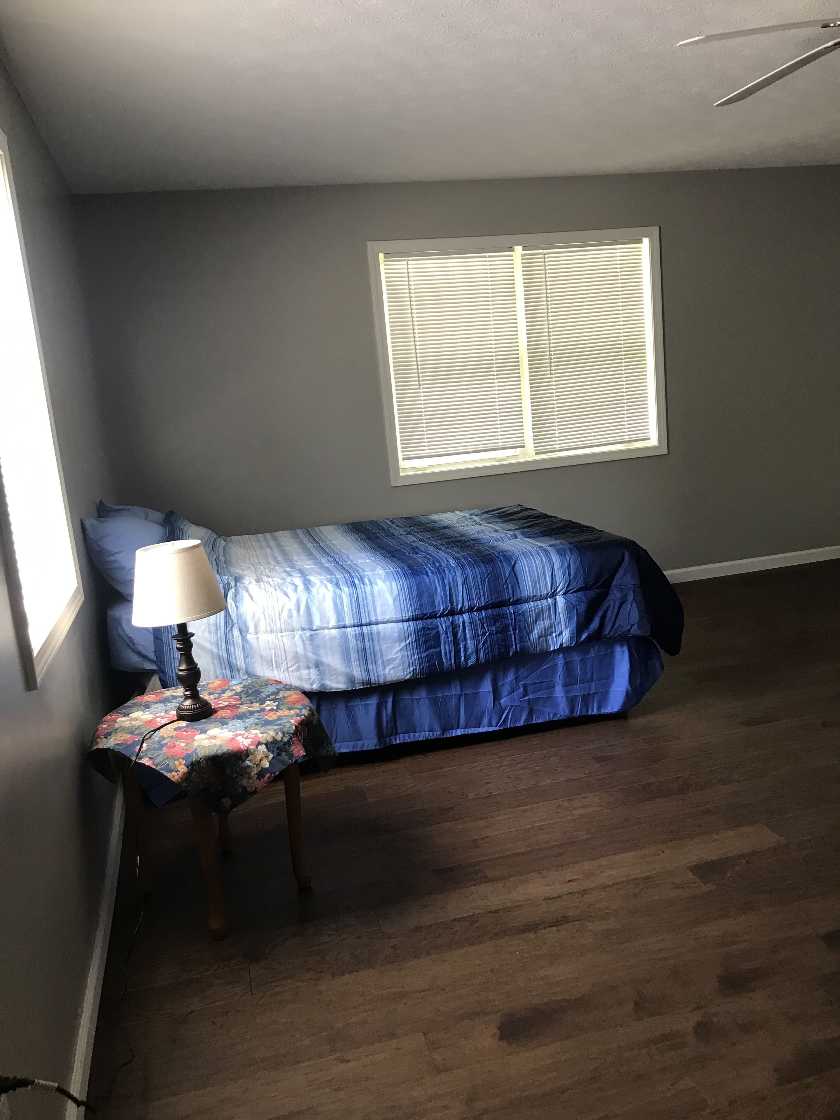 Une chambre à coucher avec un lit, une table de chevet, une lampe et une fenêtre.