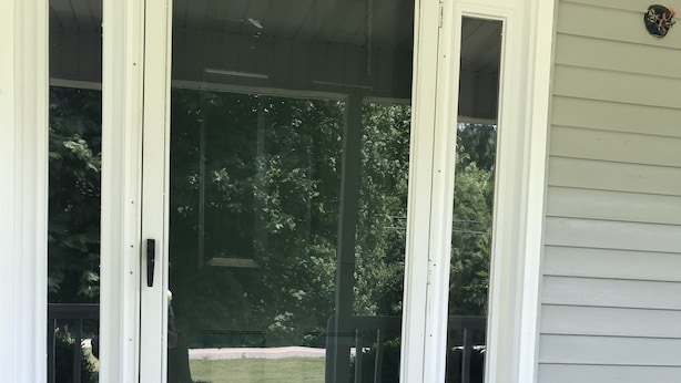 Une porte-fenêtre coulissante blanche, avec un paillasson orné d’un motif représentant un hibou.