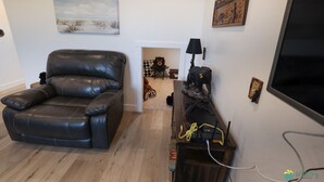 Un salon avec un canapé en cuir, une cheminée, une statue d’ours et un téléviseur fixé au mur.