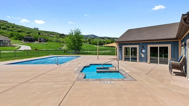 Un espace piscine comprenant deux piscines, un coin salon couvert et une vue sur un paysage vallonné.
