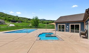 A pool area with two pools, a covered seating area, and a view of a hilly landscape.