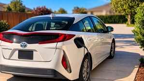 A white Toyota Prius Prime parked on a driveway with a charging cable connected.