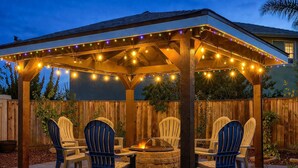 A covered patio area with string lights, a fire pit, and outdoor seating.