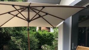 Une terrasse avec un canapé, deux fauteuils à bascule, une table et un grand parasol.