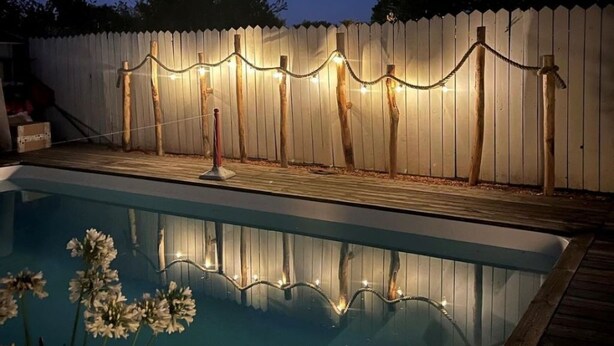 Une piscine dotée d’une terrasse en bois et entourée d’une clôture blanche en piquets, agrémentée de guirlandes lumineuses.