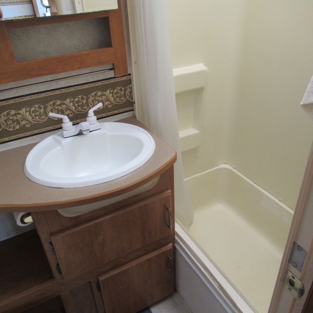 Un baño con un lavamanos blanco, un mueble de madera y una zona de ducha.