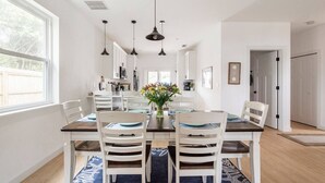 Un espace repas avec une table en bois, des chaises blanches et des lampes suspendues.