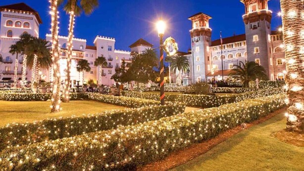 Une cour d’hôtel bien éclairée, avec une fontaine centrale, des palmiers et un jardin soigné, le tout illuminé la nuit.