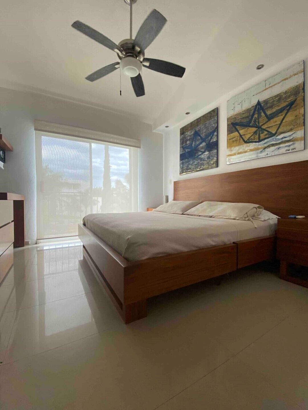 A bedroom with a bed, a ceiling fan, and artwork on the wall.
