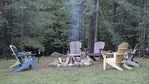 A campsite with a fire, several Adirondack chairs, and a picnic table. - Luxury Mnt. View Cabin with game room, hot tub, fire pit and private ski trails (Au Sable Forks)