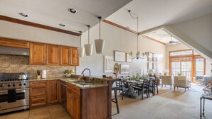 Une cuisine spacieuse dotée de meubles en bois, d’un grand îlot central et d’un coin repas offrant une vue sur l’extérieur.