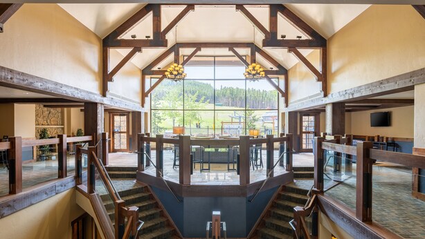 Un intérieur spacieux avec un escalier central, de grandes fenêtres offrant une vue sur l’extérieur, et un coin salon avec des tables et des chaises.
