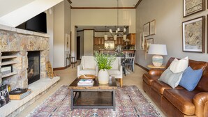 Un salon spacieux avec une cheminée en pierre, un canapé en cuir et une table basse agrémentée de livres et d’une plante.