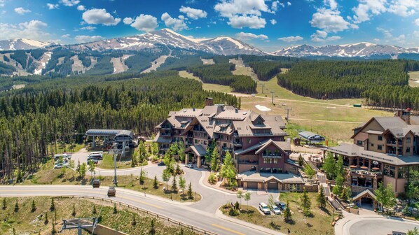 A mountain lodge with a ski lift, surrounded by forest and mountains.