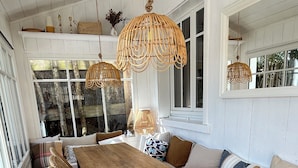 Een eetruimte met een houten tafel, rieten stoelen en hangende rotan lampen.