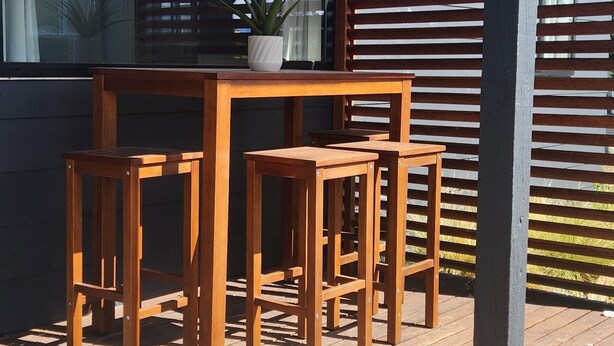 A wooden deck with a table and chairs, a potted plant, and a metal railing.