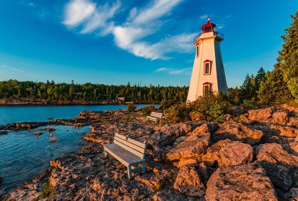 Un phare se dresse sur une côte rocheuse, offrant une vue dégagée sur la forêt et l’étendue d’eau environnantes.