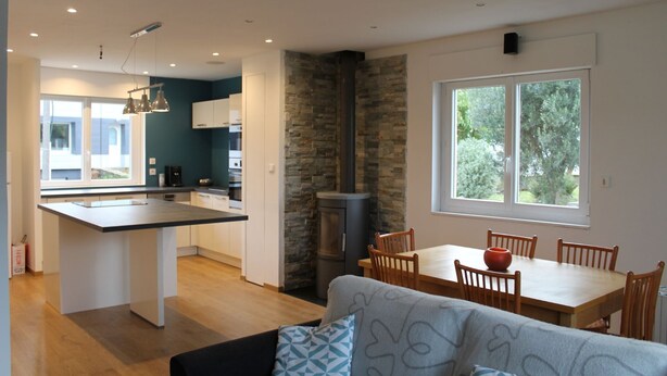 Una cocina moderna con una isla central, un comedor con un amplio ventanal y una zona de estar acogedora con cojines estampados.