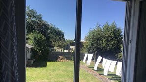 Una ventana con vista a un patio cubierto de césped, árboles y una valla.
