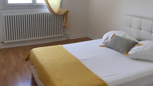 Un dormitorio con cama, una ventana con cortinas, un radiador y una lámpara colgante.