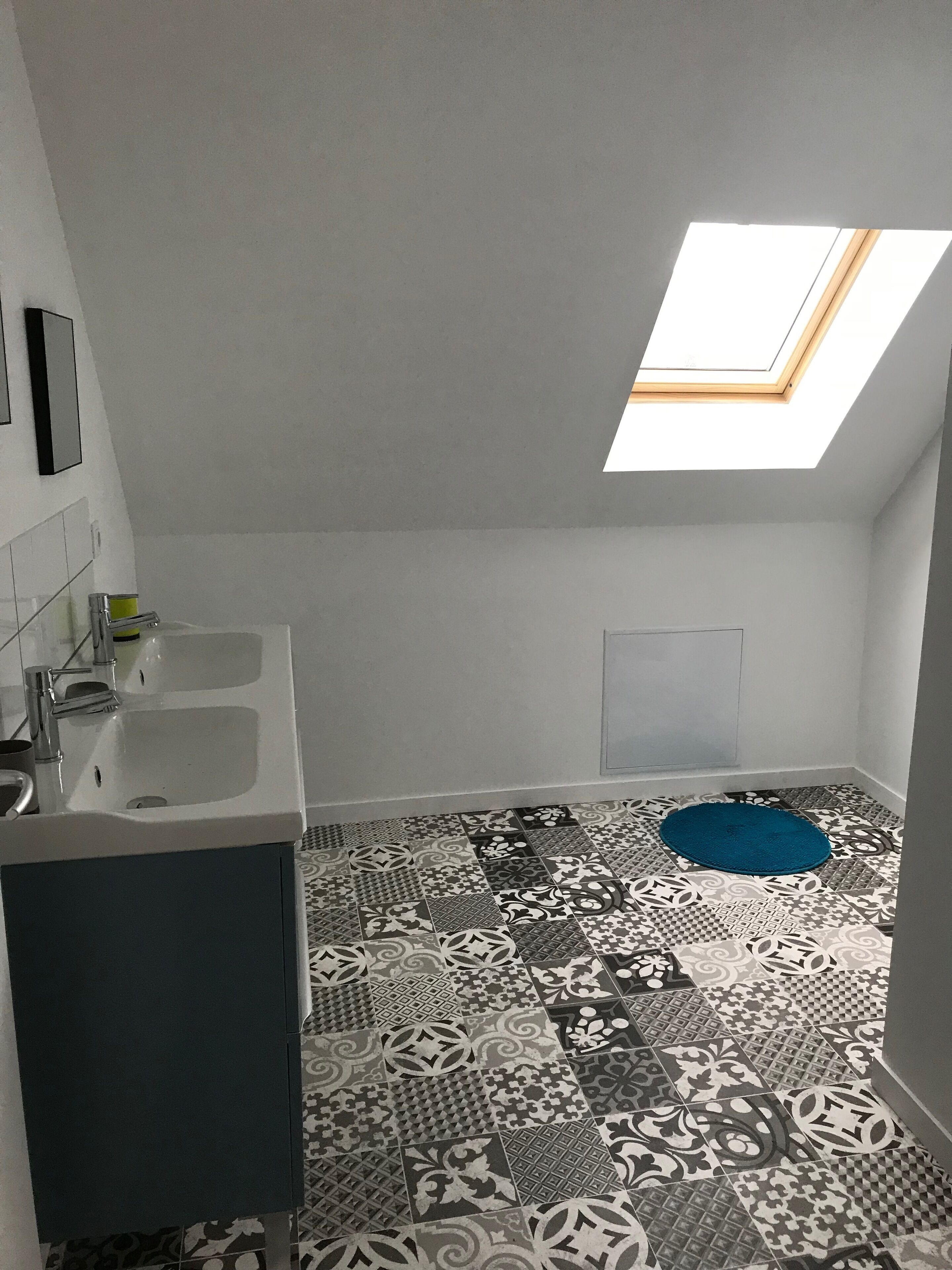 A bathroom with a skylight, two sinks, patterned floor tiles, and a blue rug.