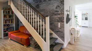 Una sala de estar moderna con una escalera, un sofá rojo, una estantería y una cocina al fondo.