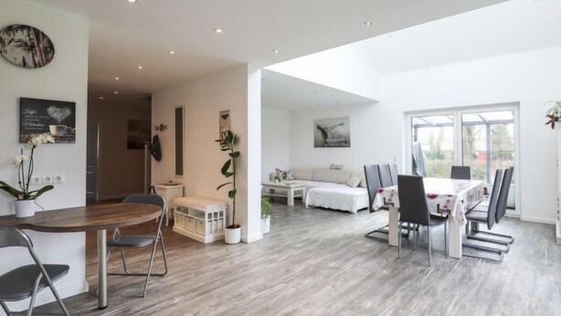 Un salón amplio con mesa de comedor, sillas, sofá y una mesa de centro. Hay un ventanal grande que proporciona luz natural y vistas al exterior.