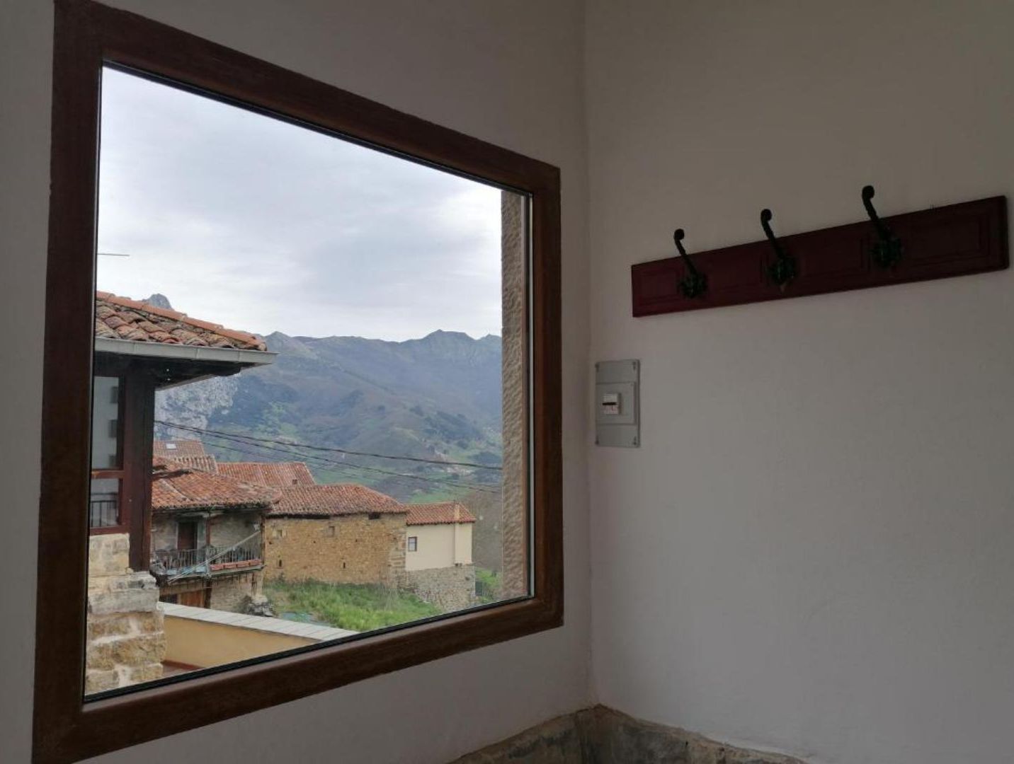 Une pièce dotée d’une grande fenêtre donnant sur un paysage montagneux et des bâtiments traditionnels.