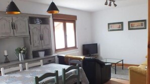A dining area with a table and chairs, a kitchen with cabinets, a television, and a sofa. - Casa el Enebral (Colio)