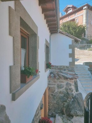 Una estrecha escalera de piedra que lleva a una puerta, con una ventana a la izquierda y una pared blanca.
