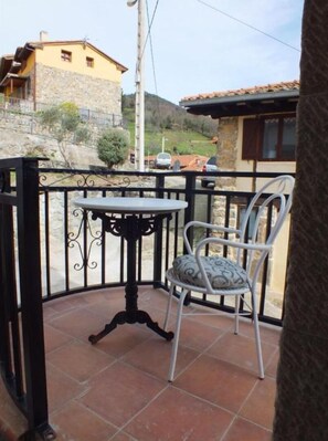 Un balcon avec une table et une chaise, un mur en pierre et un bâtiment en arrière-plan.