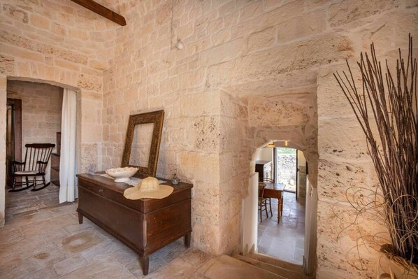 A rustic stone-walled room with a wooden dresser, a mirror, and a wicker basket. - WePuglia - Trullo Sentimento (Martina Franca)