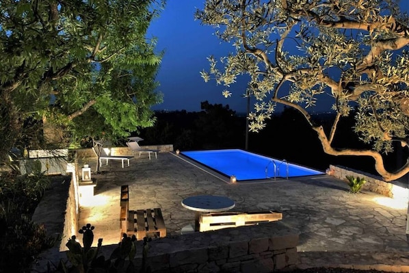 A stone pool with a blue cover, surrounded by a stone patio and a large tree.