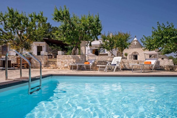 A swimming pool with lounge chairs and a stone building in the background.