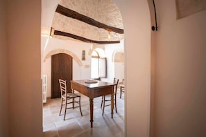 A dining area with a wooden table and chairs, stone walls, and an arched doorway.