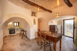 A rustic kitchen with stone walls, a wooden table, and a view through a glass door.