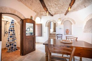 Ein rustikales Interieur mit einem Holzespeisetisch, Steinwänden und Blick in einen Küchenbereich.